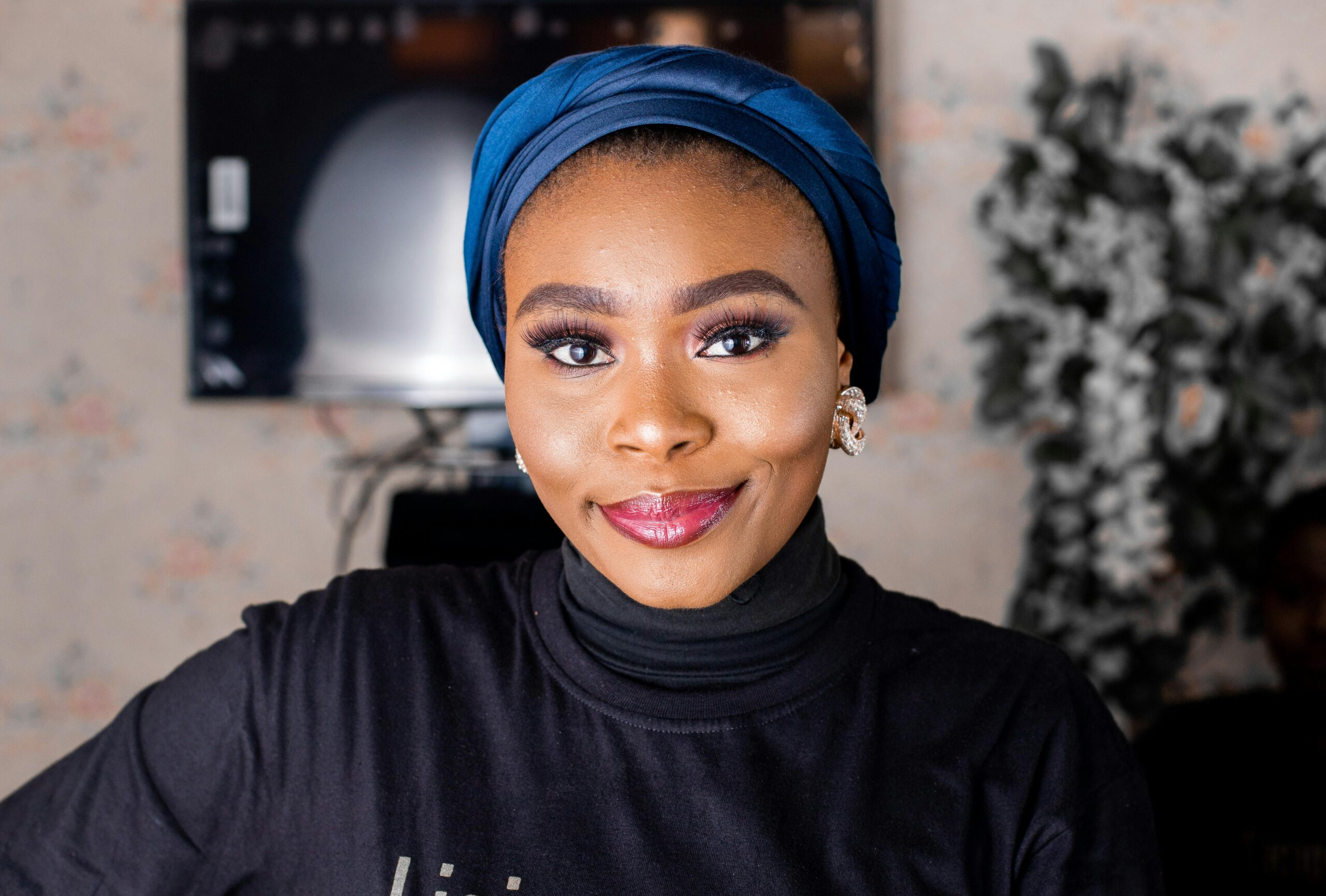 Home Vibrant portrait of a smiling woman indoors wearing a blue turban and stylish black turtleneck.